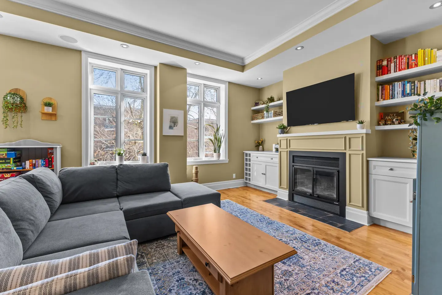 Living room with a gray sectional sofa, wood coffee table, fireplace, and built-in bookshelves. Two windows provide natural light.