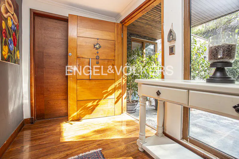 A bright foyer with a wooden door, hardwood floors, and a white console table. Sunlight streams in, highlighting the Engel & Volkers logo on the door.