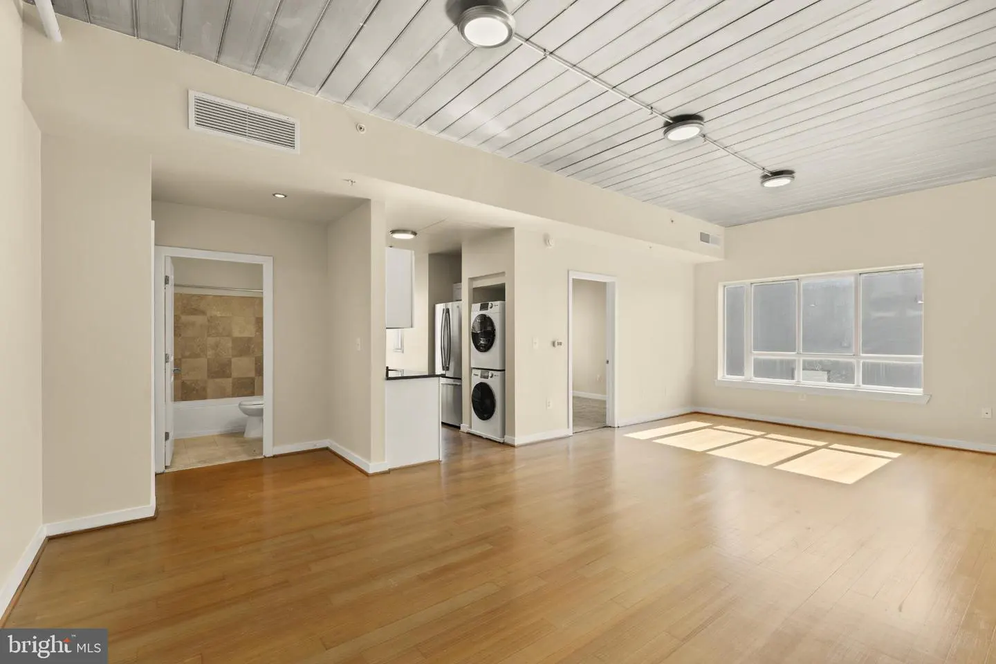 Bright, open apartment with hardwood floors, white walls, and a modern kitchen with stainless steel appliances and in-unit laundry.