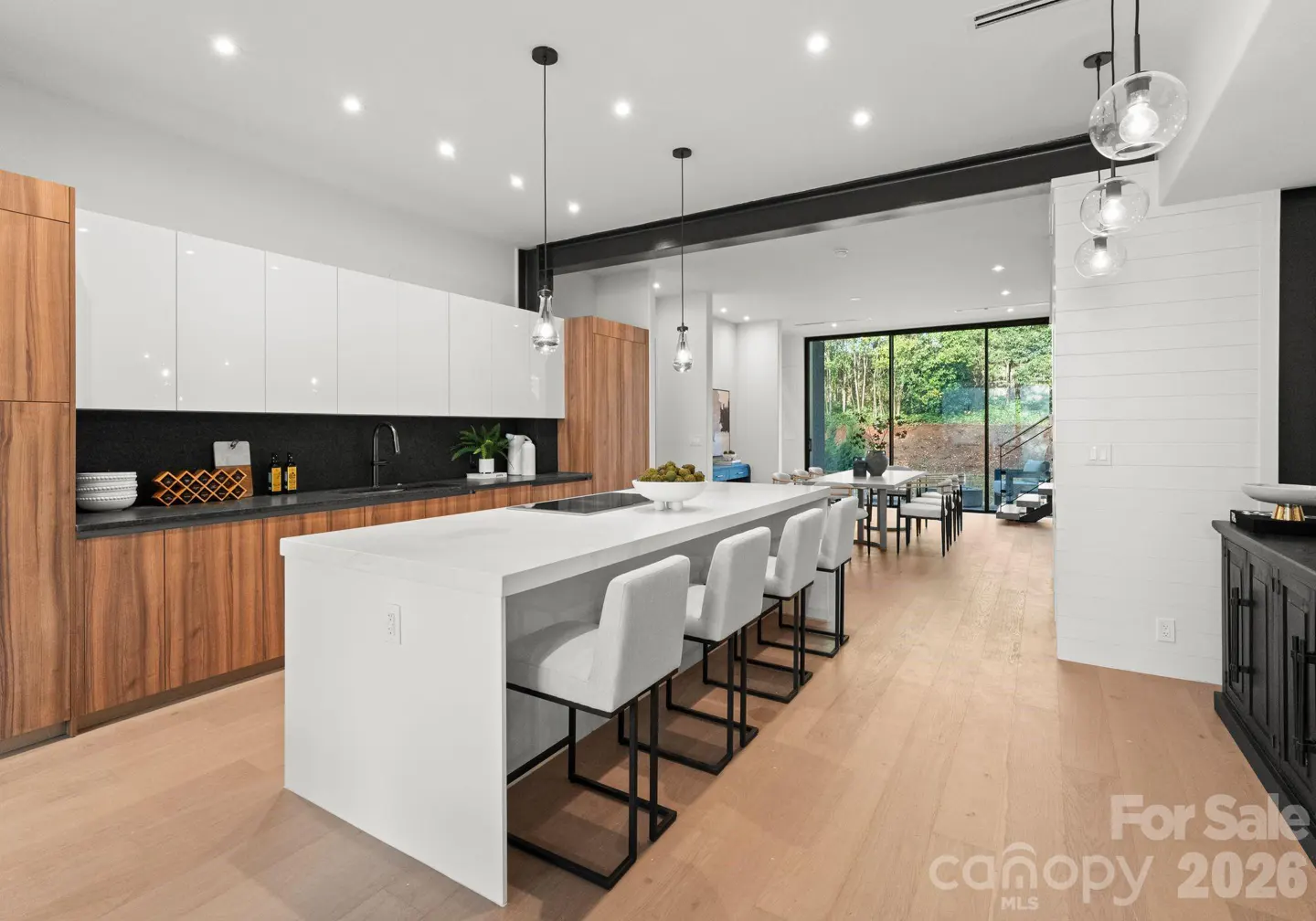 Modern kitchen with white island, four bar stools, wood cabinets, and large glass doors opening to a patio.