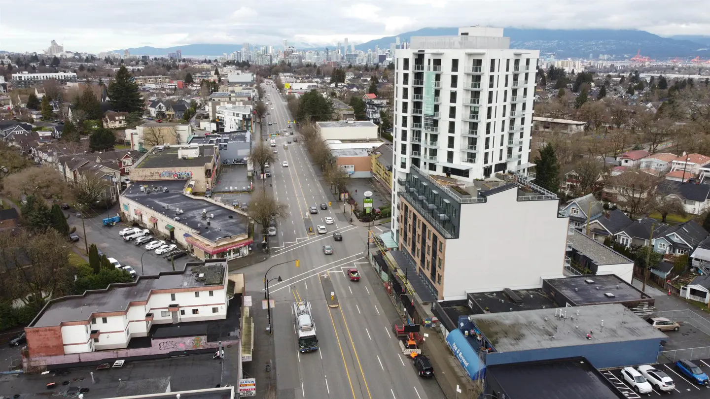 Aerial view of a city street with cars, buildings, and mountains in the background on a cloudy day.