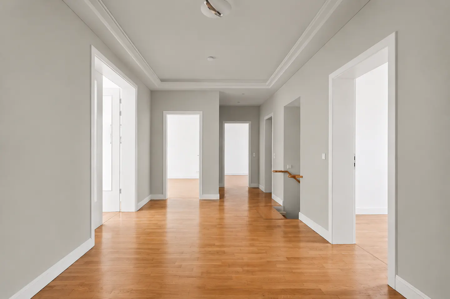 A bright hallway with light gray walls, white trim, and a glossy wood floor. Several open doorways lead to other rooms.
