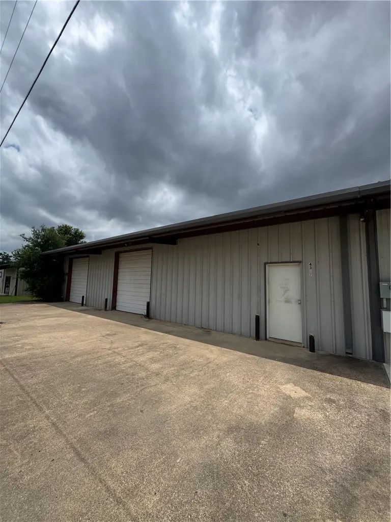 Exterior view of a long, grey metal industrial building with two white roll-up doors and a white entry door under a cloudy sky.