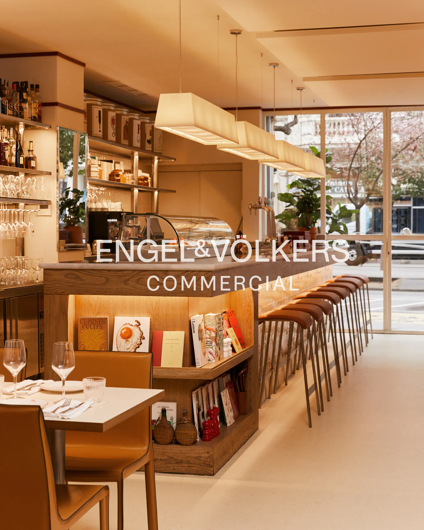 A bright, modern restaurant interior with a bar, stools, and a set table. Engel & Völkers Commercial logo is displayed.