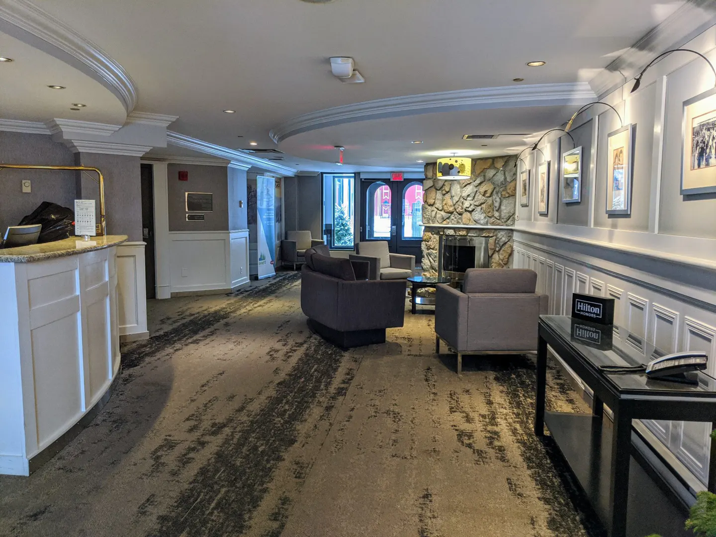 Hotel lobby with a front desk, seating area, stone fireplace, and framed pictures on the wall.