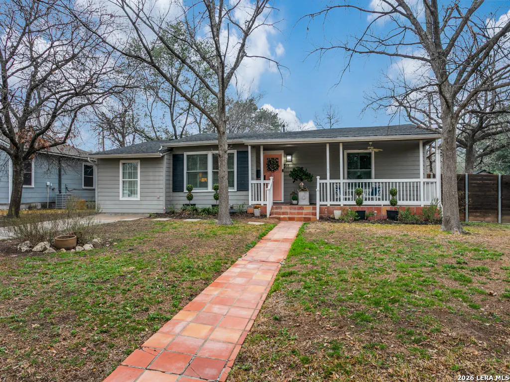A gray single-story house with a pink door and a brick walkway leading to the front porch.