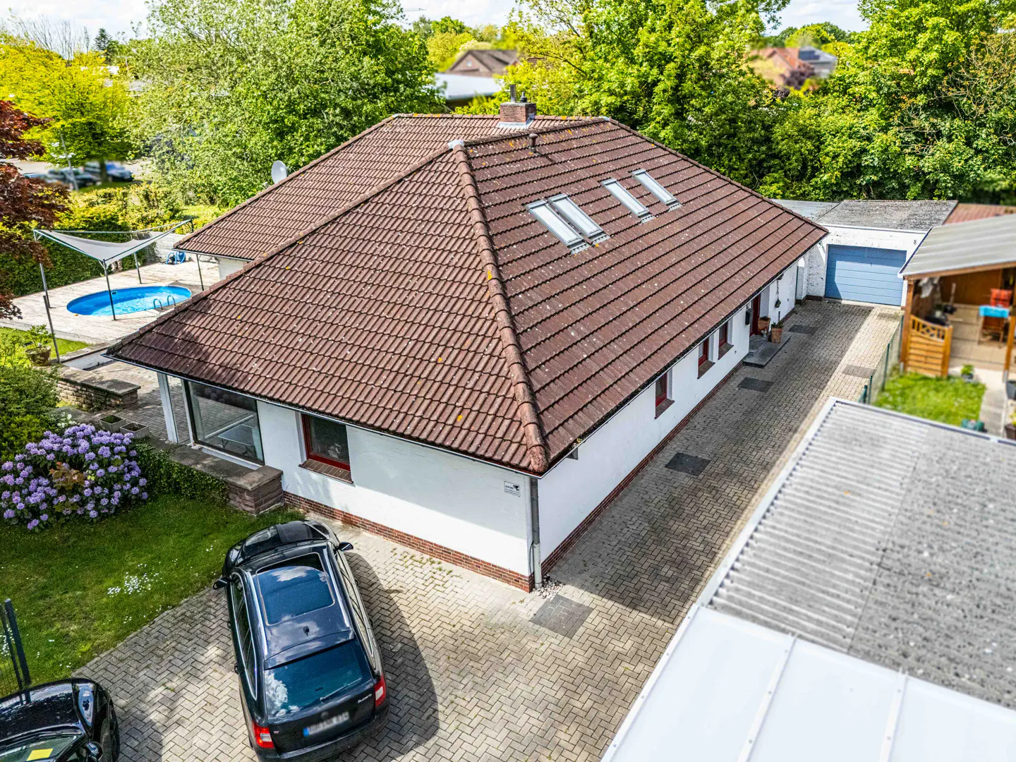 Aerial view of a white house with a brown tile roof, skylights, a pool, and two cars parked in the driveway.