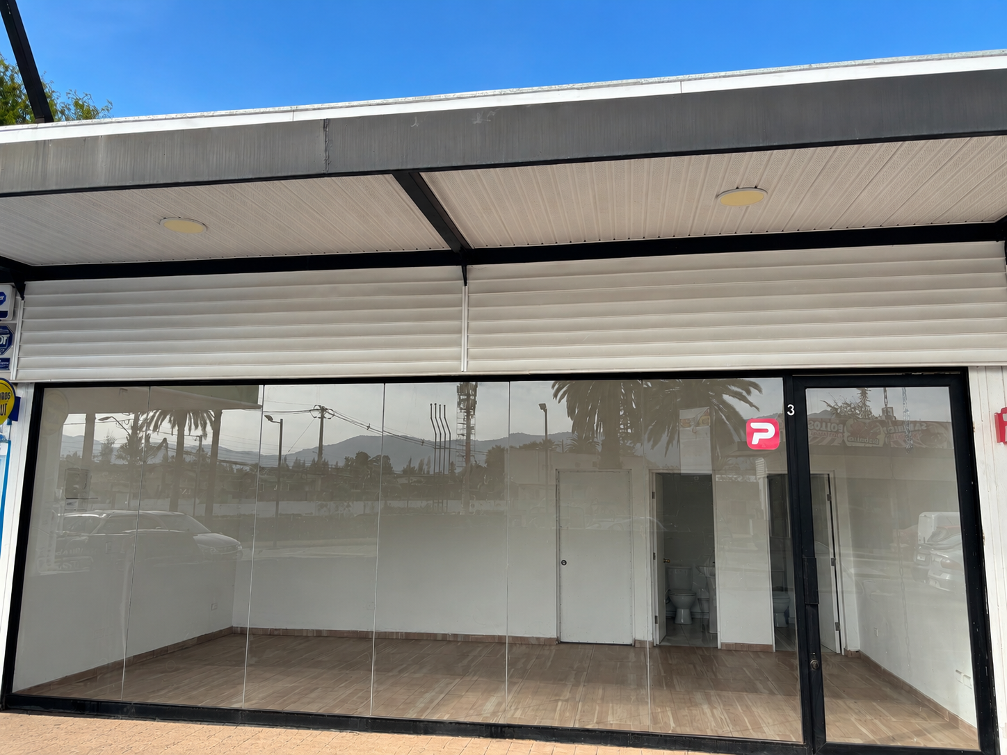 Empty commercial storefront with large glass windows, wood-look flooring, and a white interior under a modern metal awning.