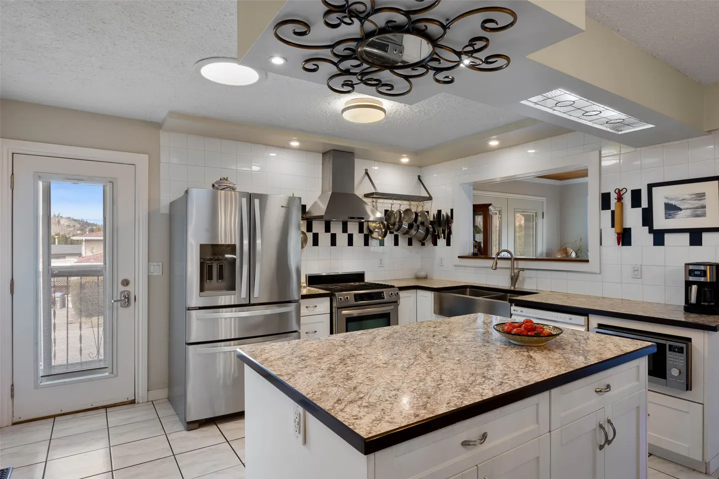 Bright kitchen with white cabinets, stainless steel appliances, and a speckled granite island. A door leads outside.
