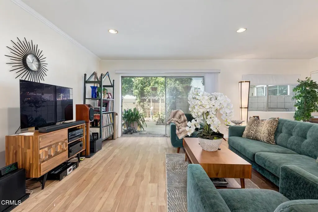 Living room with a green velvet sofa, wood floors, and a sliding glass door to a patio. A TV and bookshelf are on the left.