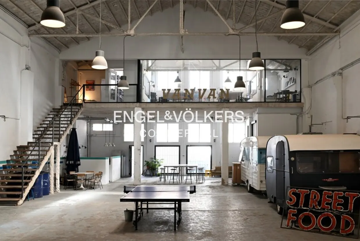 Spacious industrial office with high ceilings, a mezzanine, a ping pong table, and a vintage food trailer.