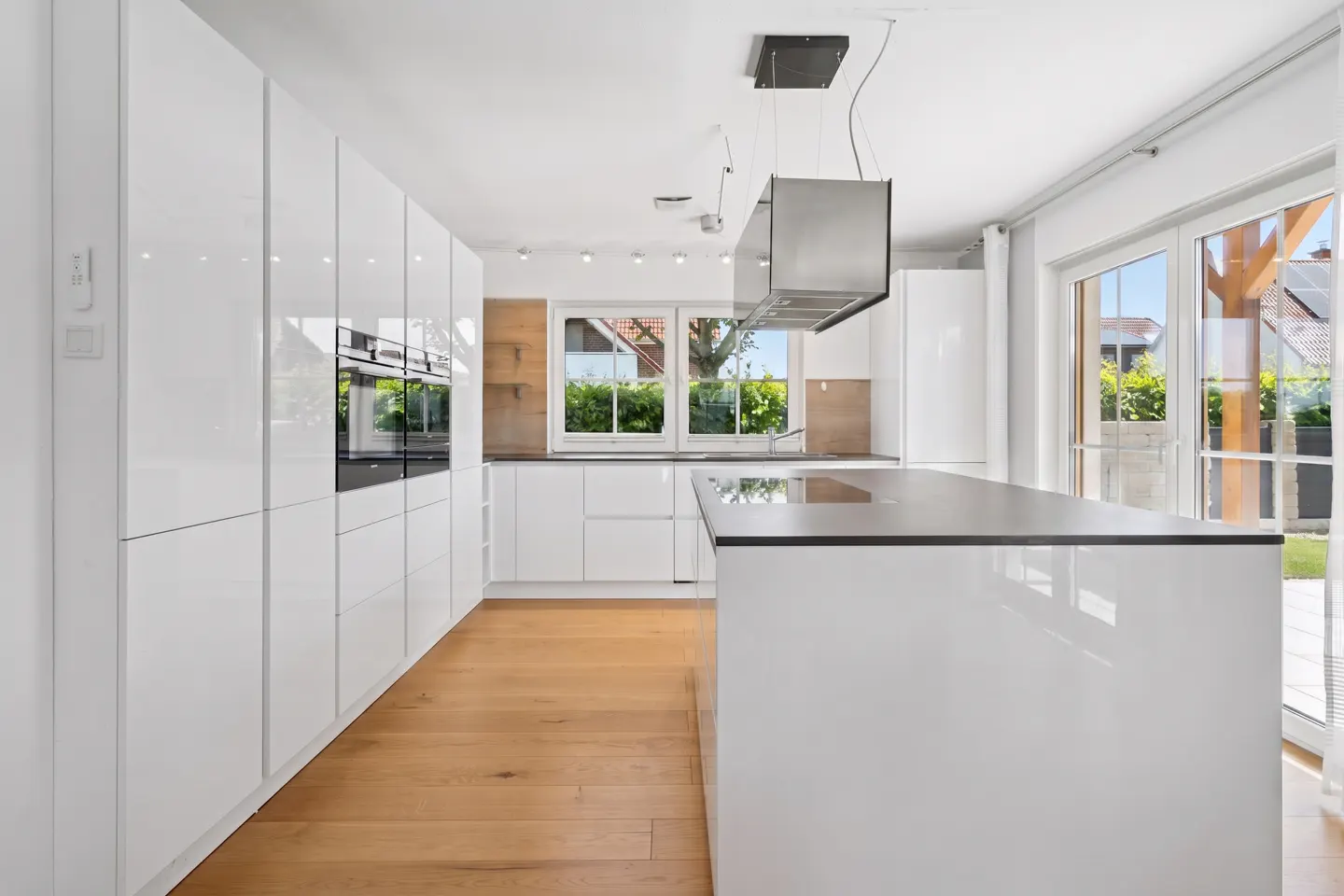 Modern kitchen with white glossy cabinets, a central island, stainless steel range hood, and light wood flooring.