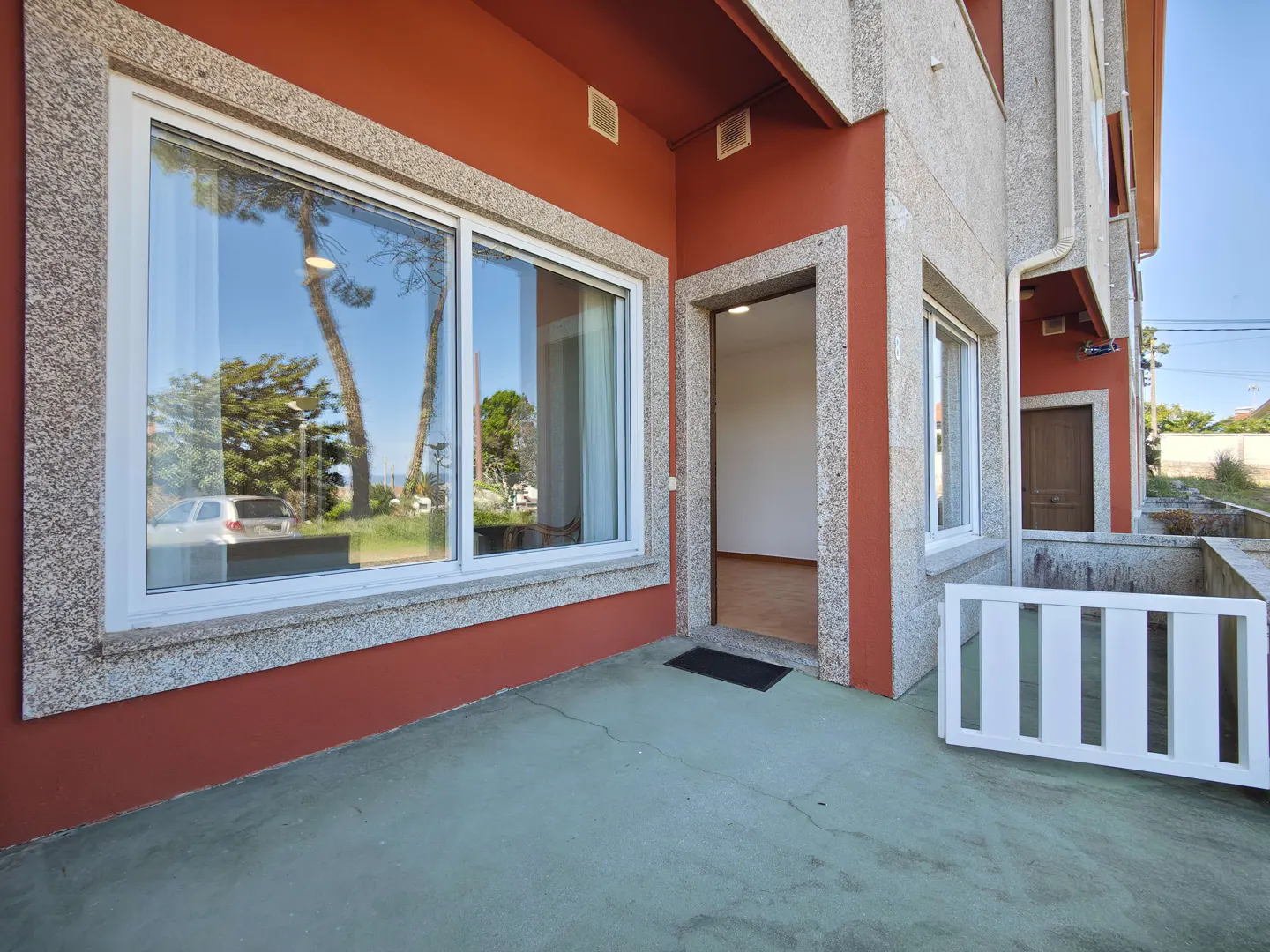 Exterior view of a two-story house with red walls, granite trim, and a large window reflecting trees and a car. An open doorway leads inside.