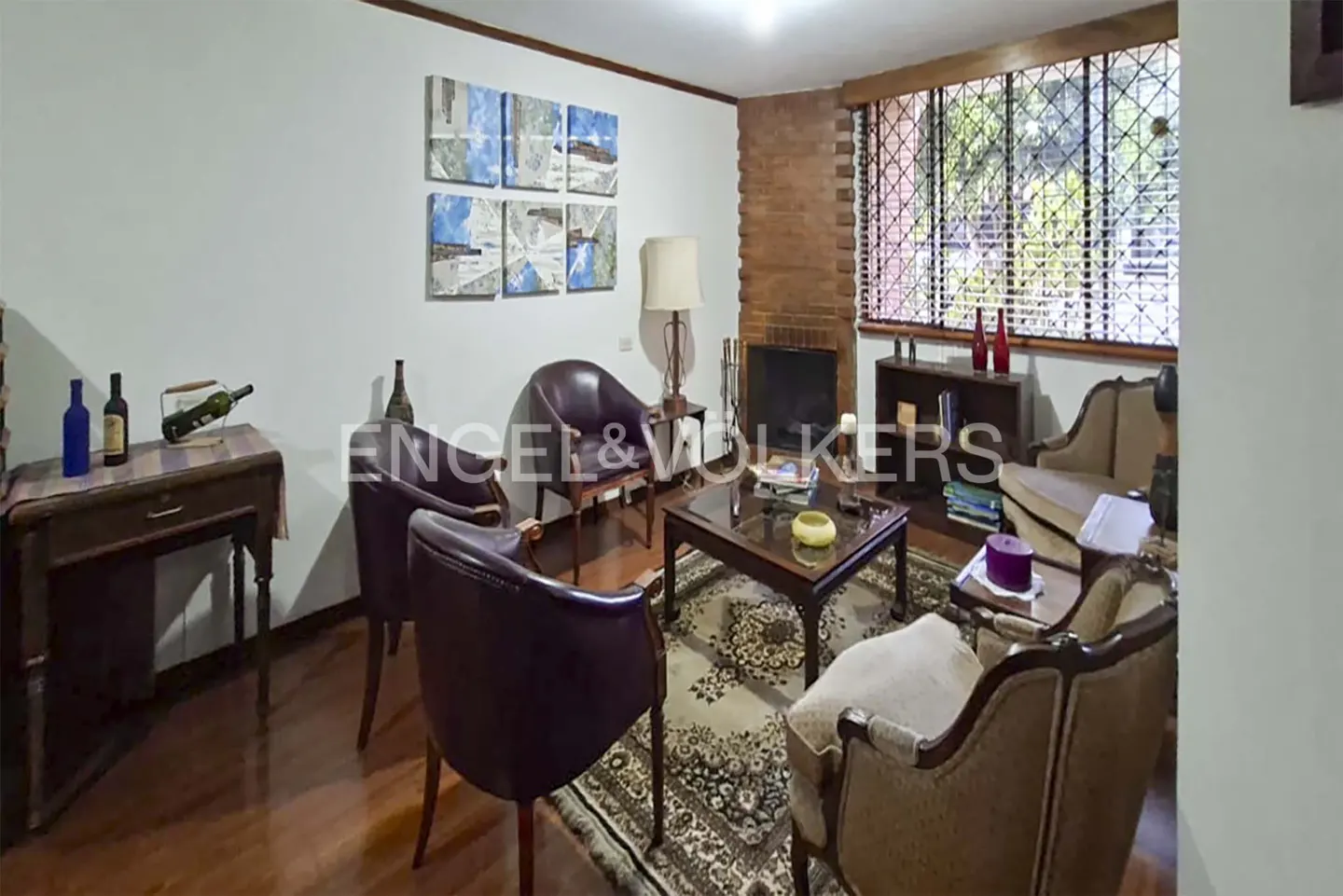 Cozy living room with dark leather chairs, a coffee table, a brick fireplace, and a large window with security bars.