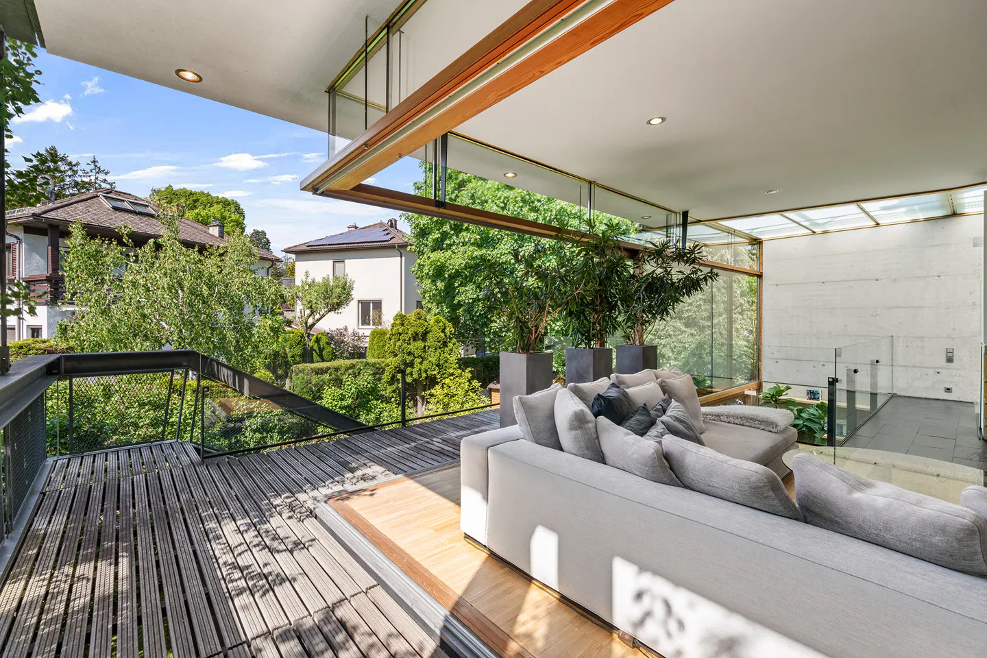 Bright living room with a gray sofa, potted plants, and a wooden deck overlooking lush greenery.