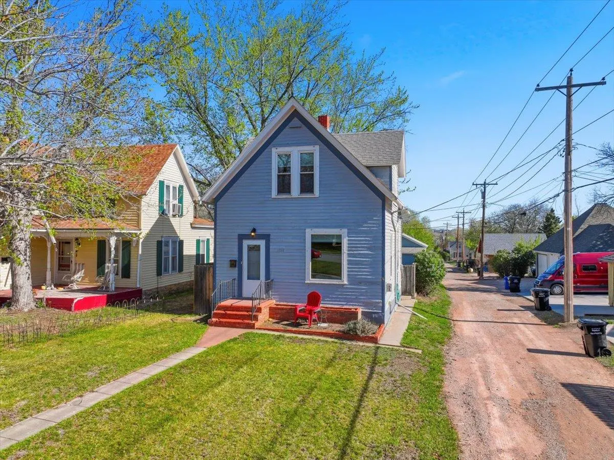 A light blue two-story house with a red chair on the porch, next to a yellow house with green shutters.