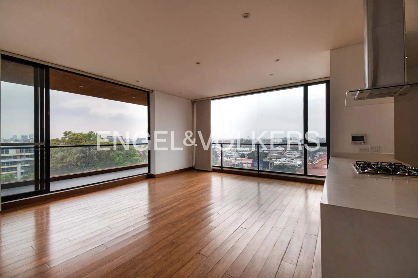 Bright, modern apartment with hardwood floors, floor-to-ceiling windows, and a white kitchen counter with a gas stovetop. City view.