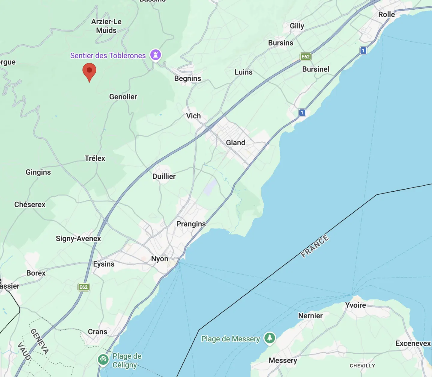 Map view of Genolier, Switzerland, with a red pin marker in a wooded area near "Sentier des Toblerones." Lake Geneva is visible in the background.