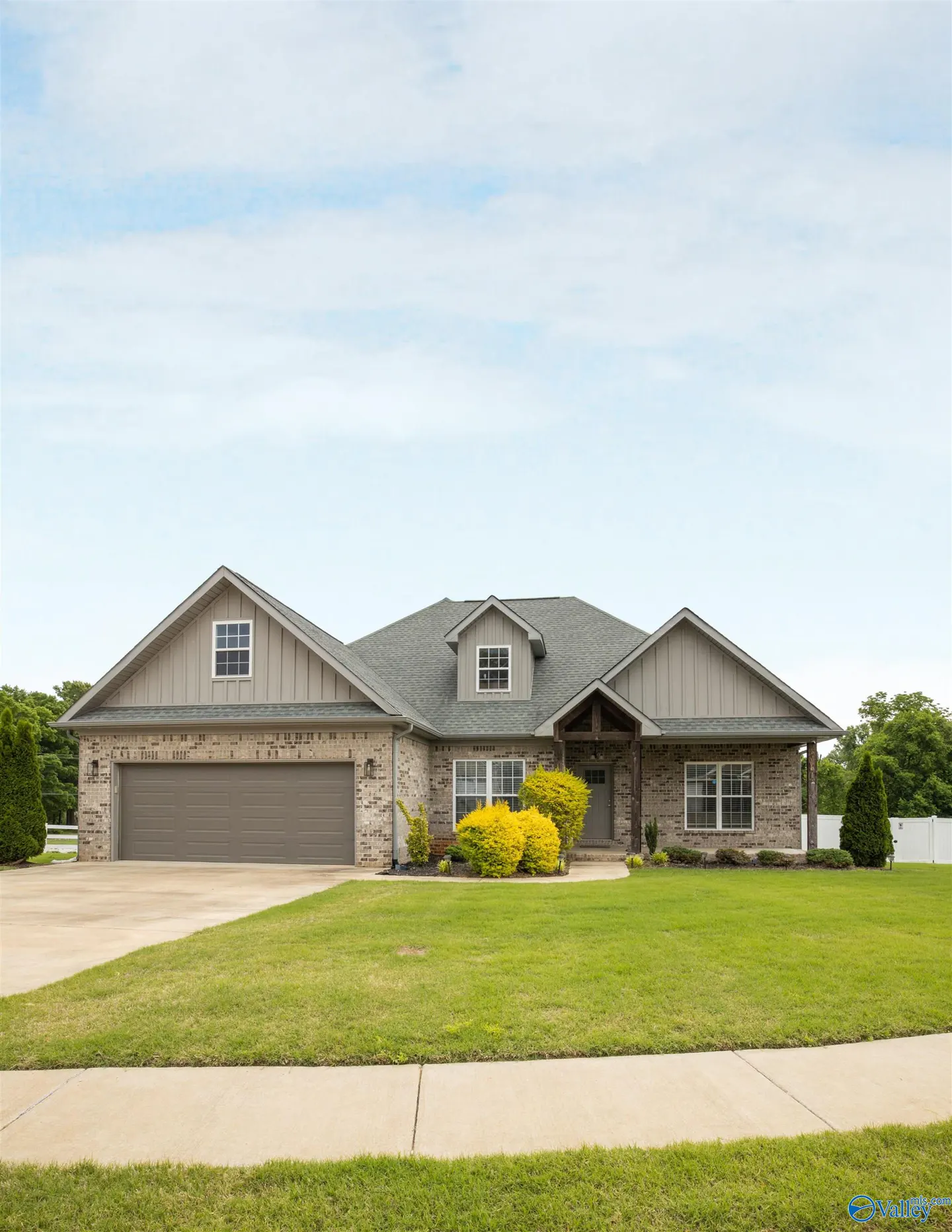 A single-story brick house with a gray roof, a green lawn, and a blue sky.