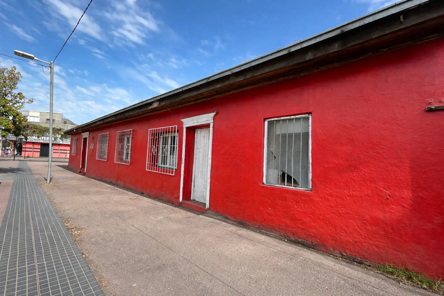 A long, bright red building with white trim and barred windows sits on a city street under a blue sky.