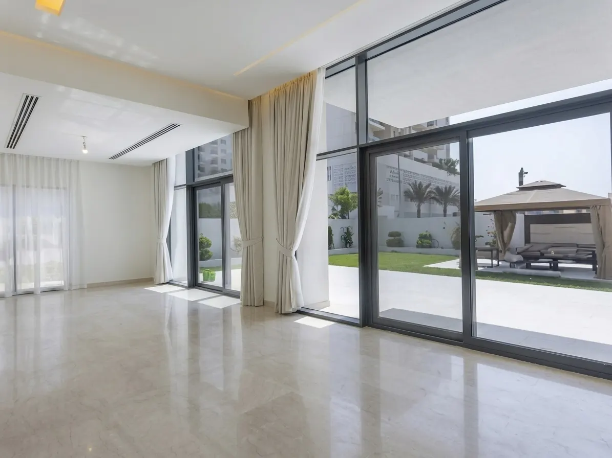 Bright, empty room with marble floors and large windows. Outside is a green lawn with a gazebo and lounge furniture.