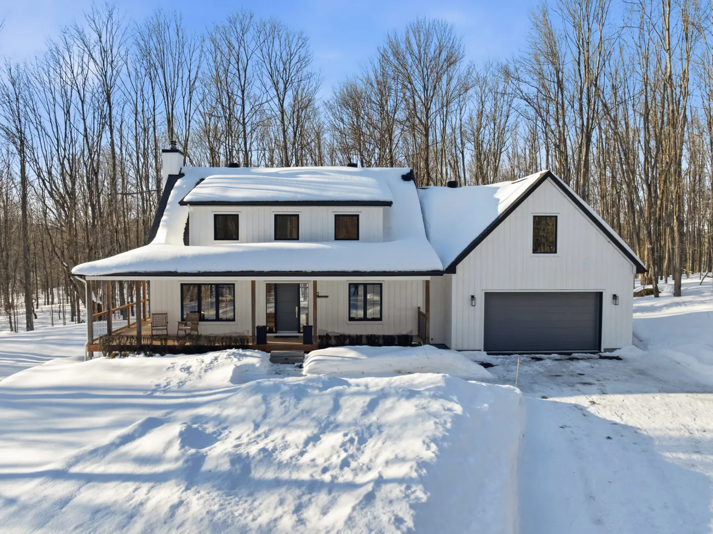 A white farmhouse with black trim and a snow-covered roof sits in a snowy landscape.