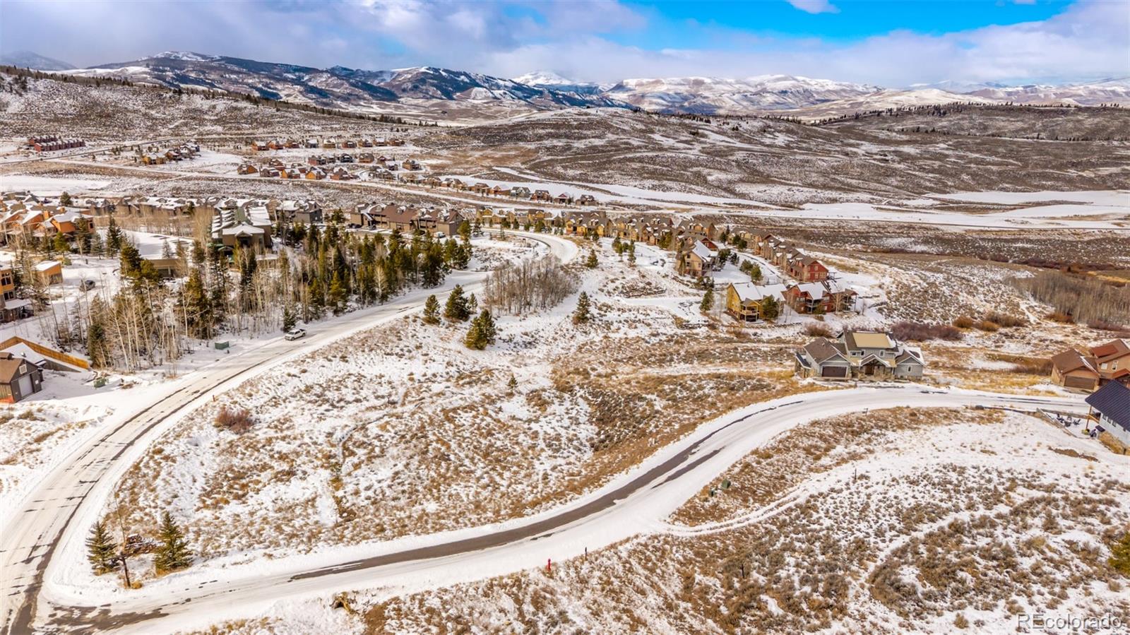 Aerial view of a snowy mountain neighborhood with winding roads, scattered houses, and distant snow-capped peaks. [AI-generated text]