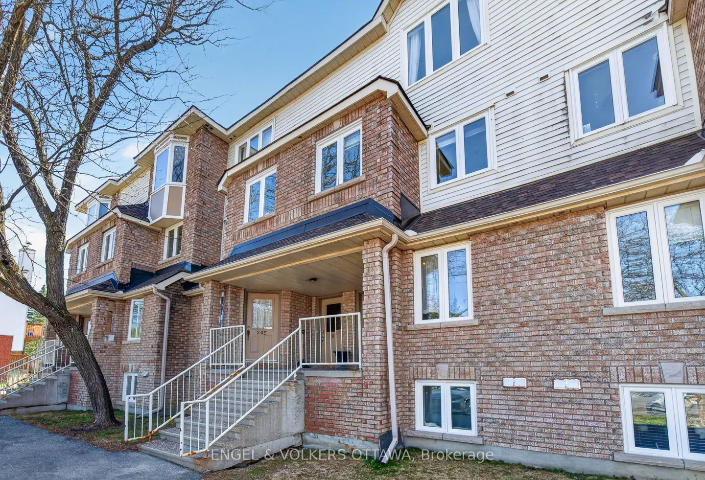 Exterior view of a brick townhouse with white trim, stairs leading to the front door, and a tree on the left.