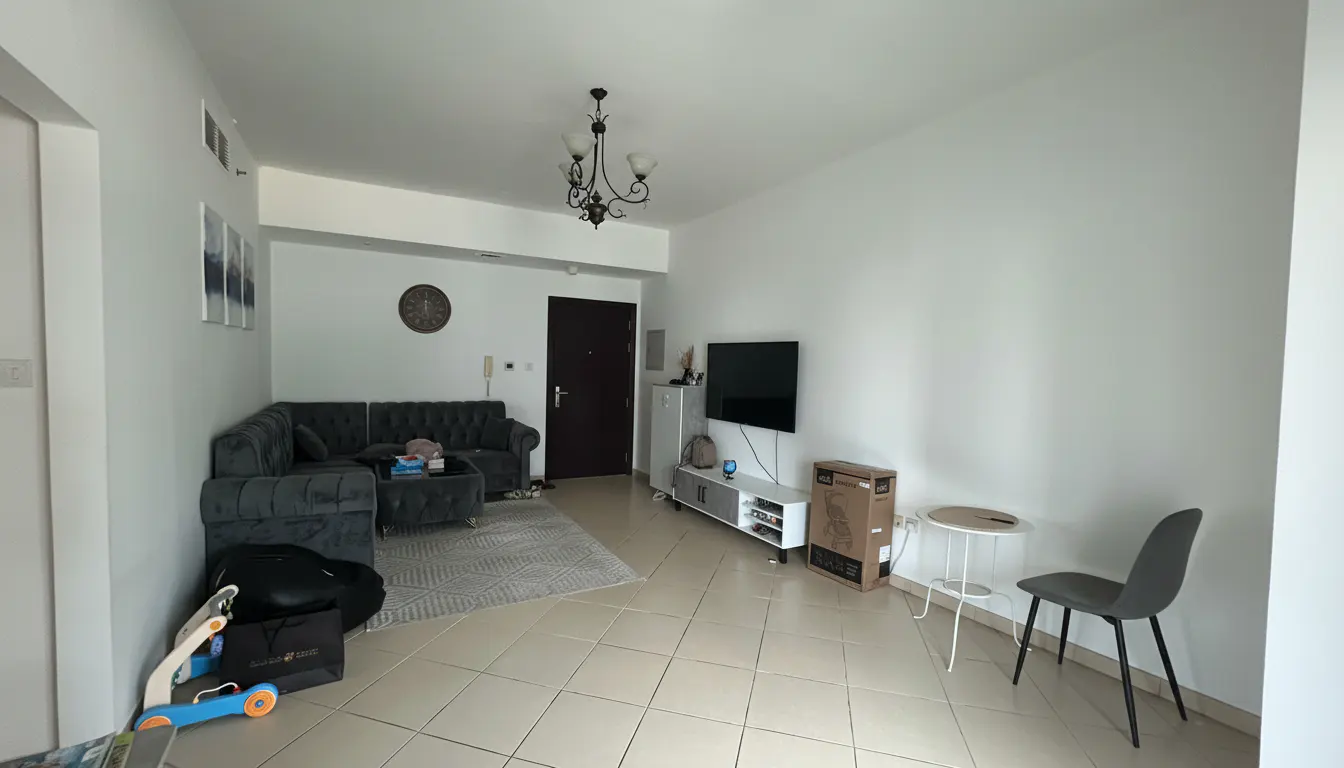 A bright living room with a gray sectional sofa, TV, and tiled floor. A chandelier hangs from the ceiling.