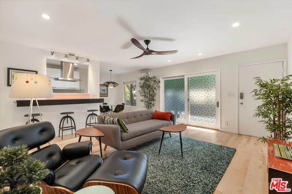 A bright living room with a gray sofa, black chair, and a green rug. A kitchen counter with stools is visible in the background.