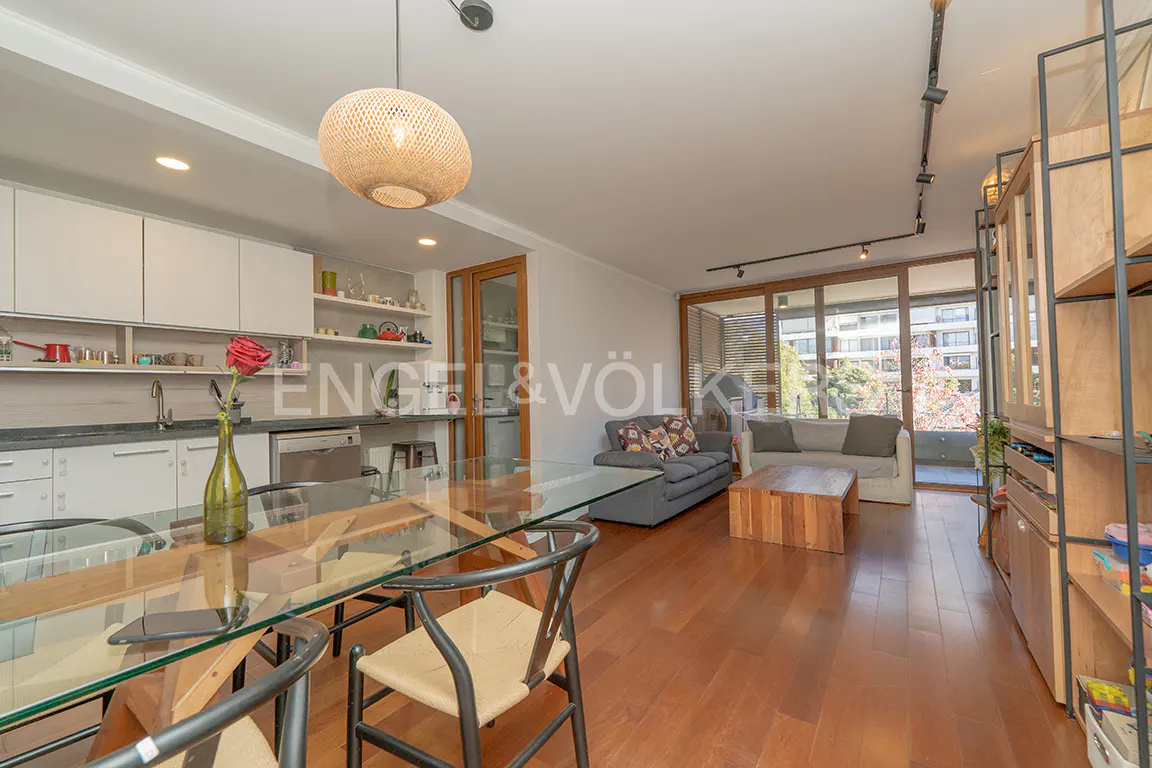 Open-concept living space with a glass dining table, wood floors, and sofas. A woven pendant light hangs above the table.