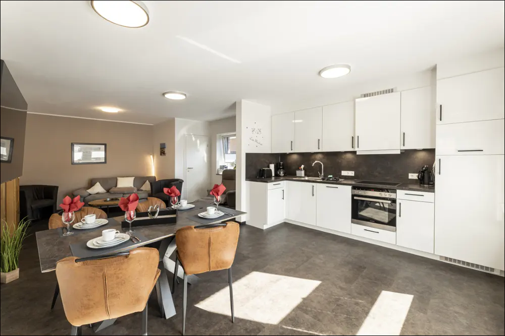 Open-concept living space with a dining table set for a meal, a modern white kitchen, and a cozy living room.