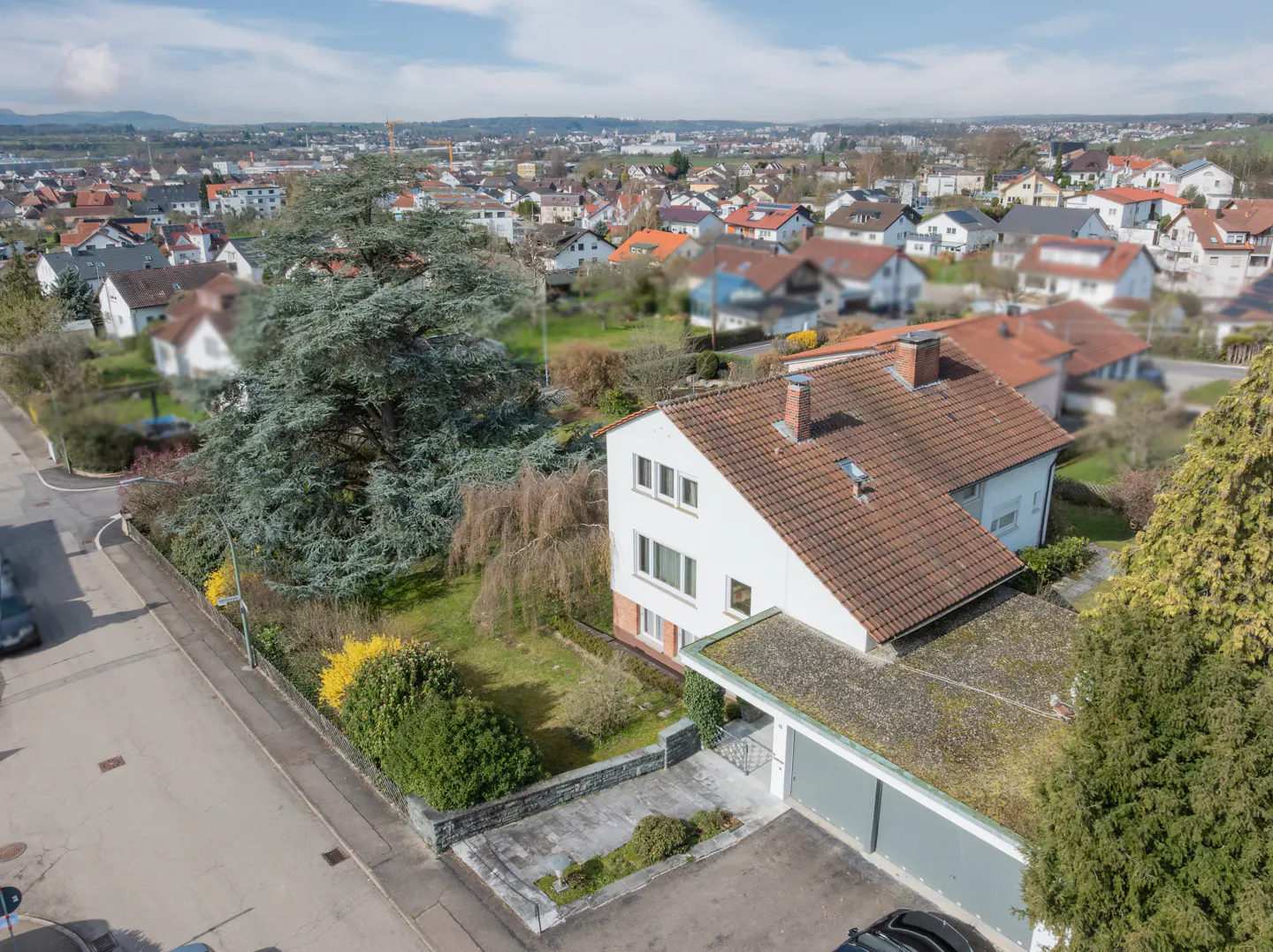 Aerial view of a white two-story house with a red tile roof, green lawn, and a two-car garage in a suburban neighborhood.