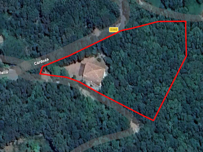 Aerial view of a property outlined in red, surrounded by dense green forest. A house with a terracotta roof sits within the property lines. Roads are visible nearby.