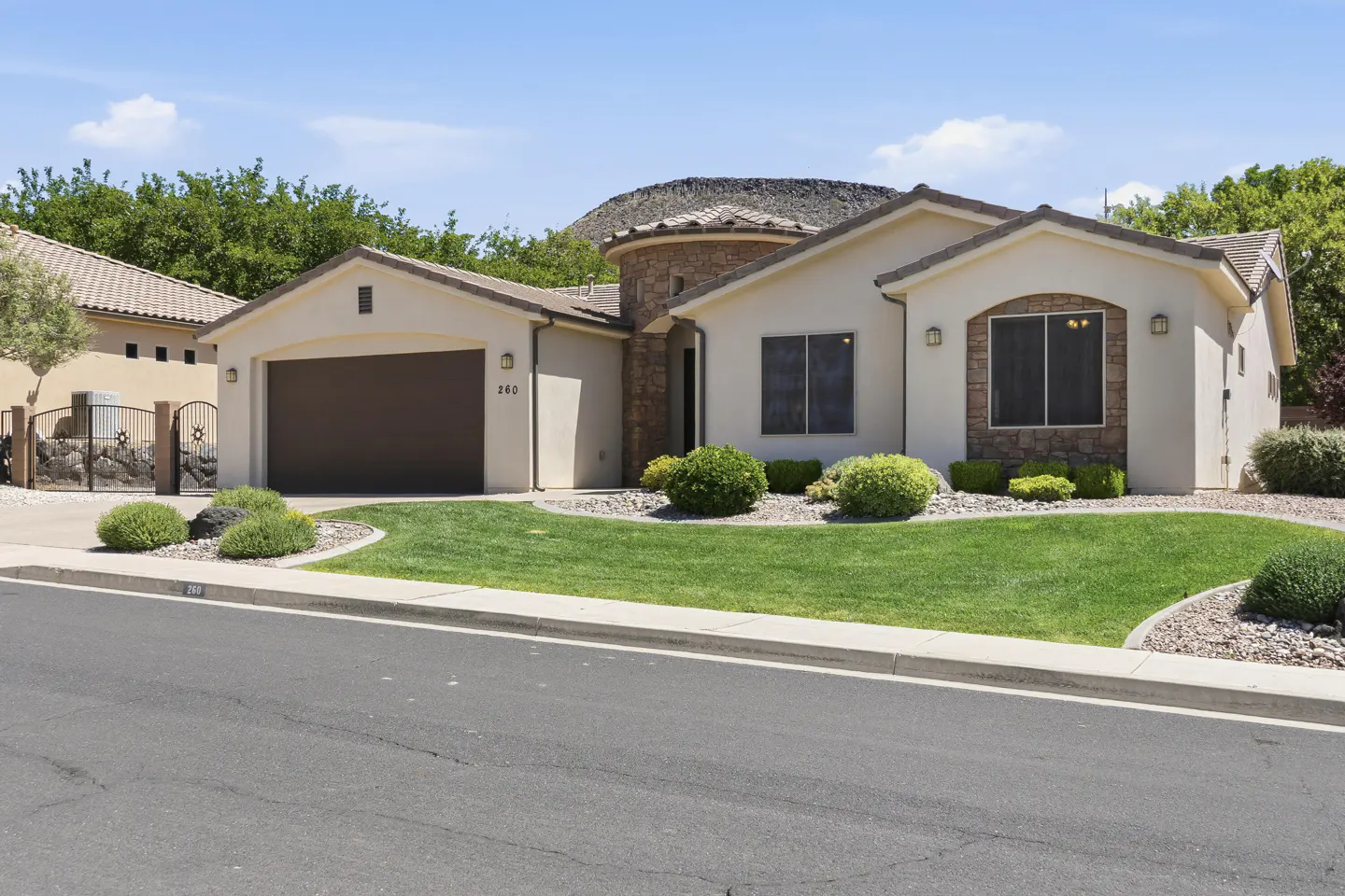 Beige single-story house with a brown garage door, a round tower, and a green lawn on a sunny day.