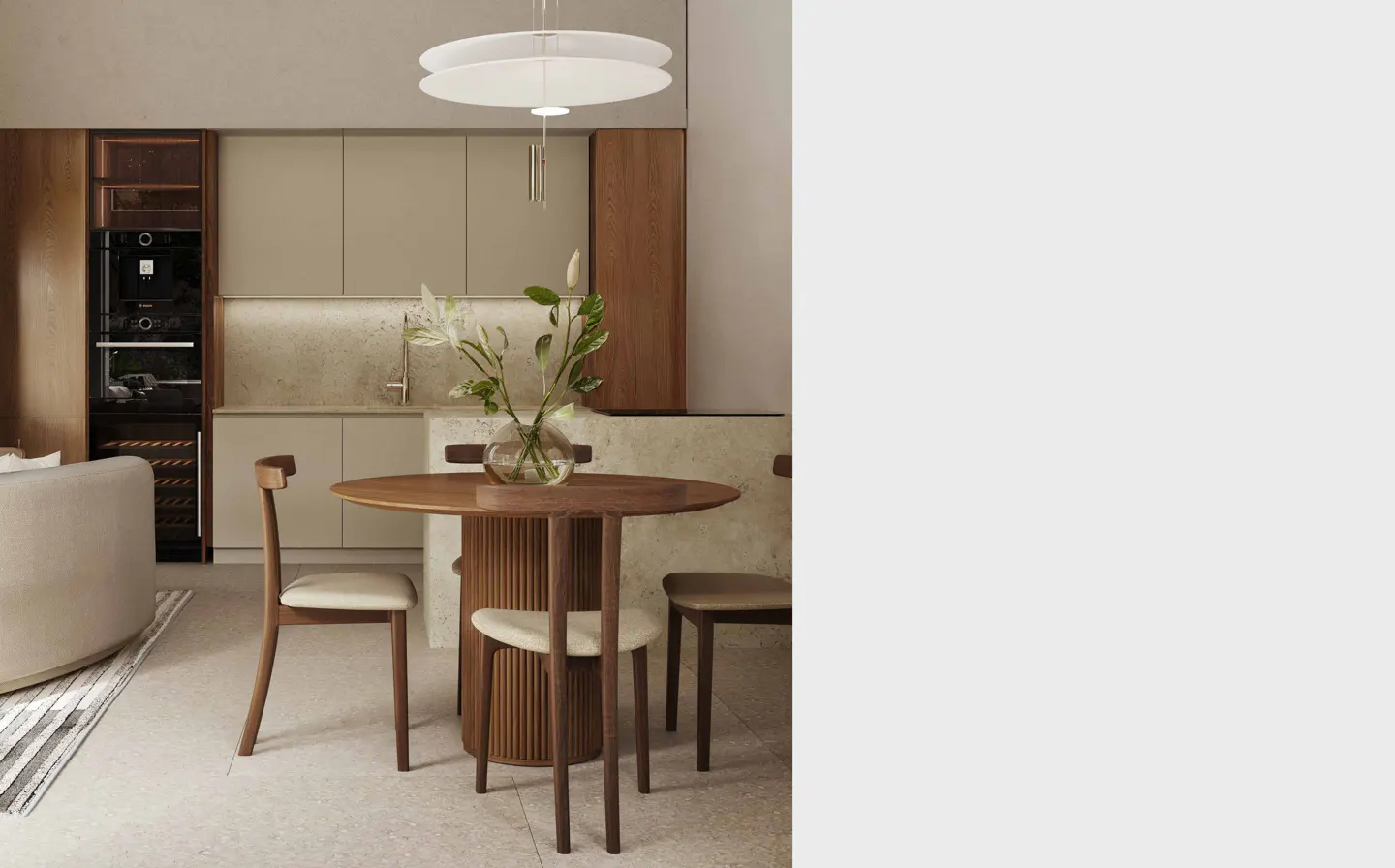 A modern kitchen with a round wooden table, chairs, and a vase of white flowers under a white pendant light.