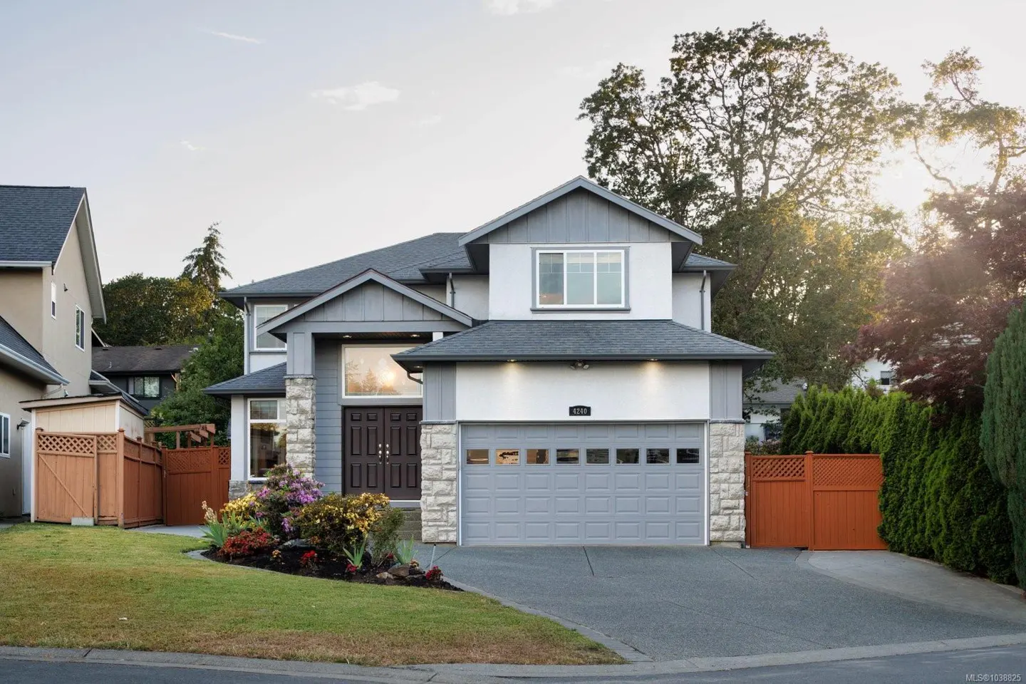 Two-story suburban home with white and grey siding, stone accents, a double garage, and a landscaped front yard.
