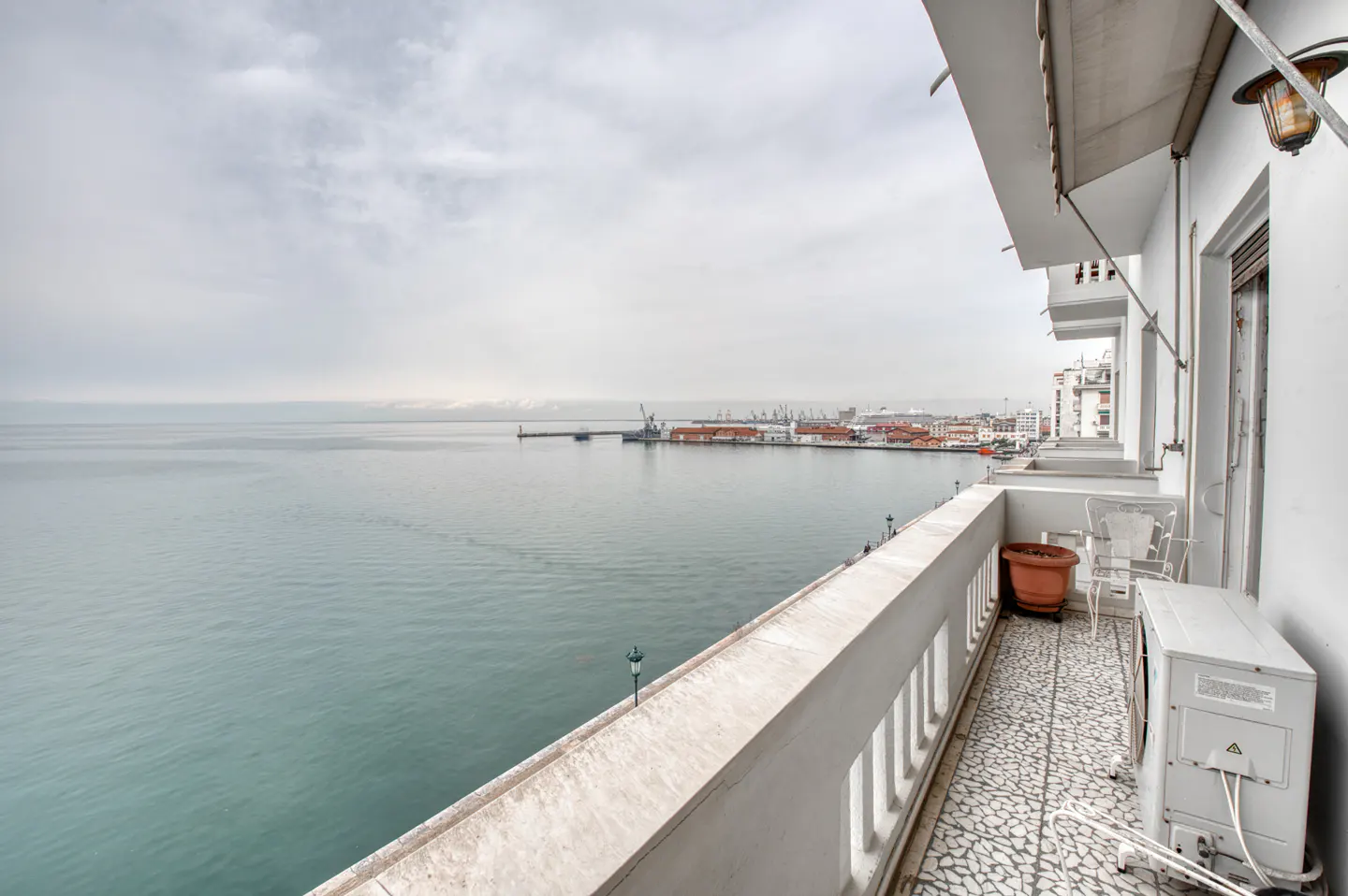 Balcony view of a harbor on a cloudy day. White railings line the balcony with a potted plant and chairs.