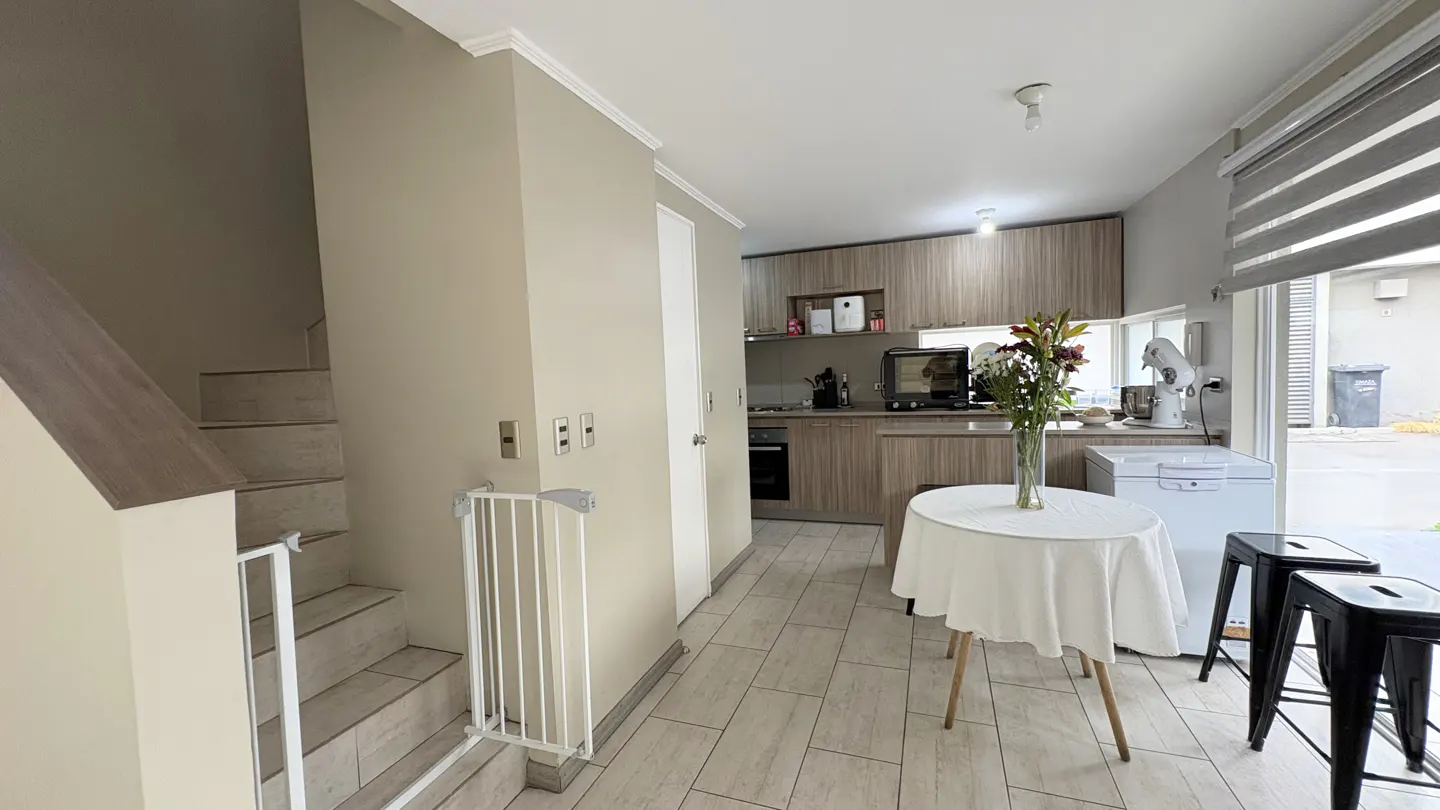 A bright, modern interior with stairs, a baby gate, and a kitchen with a round table and flowers.