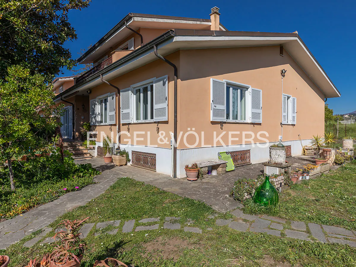 Exterior view of a peach-colored two-story house with white trim and gray shutters, surrounded by a green lawn and stone pathway.