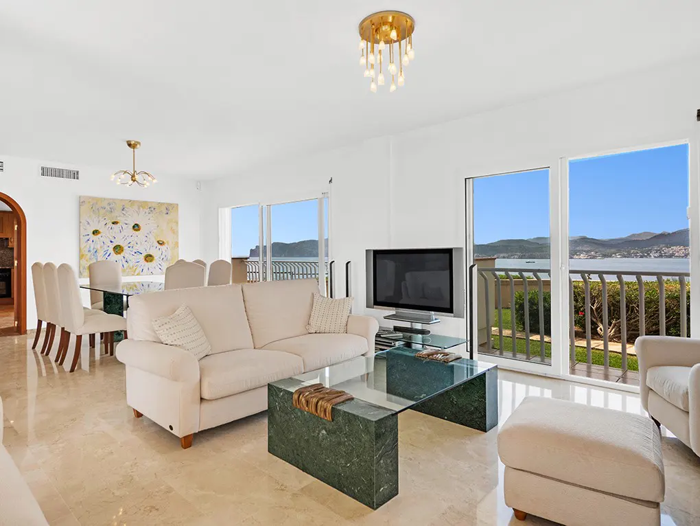 Bright living room with beige sofa, green marble table, TV, and ocean view through sliding glass doors.