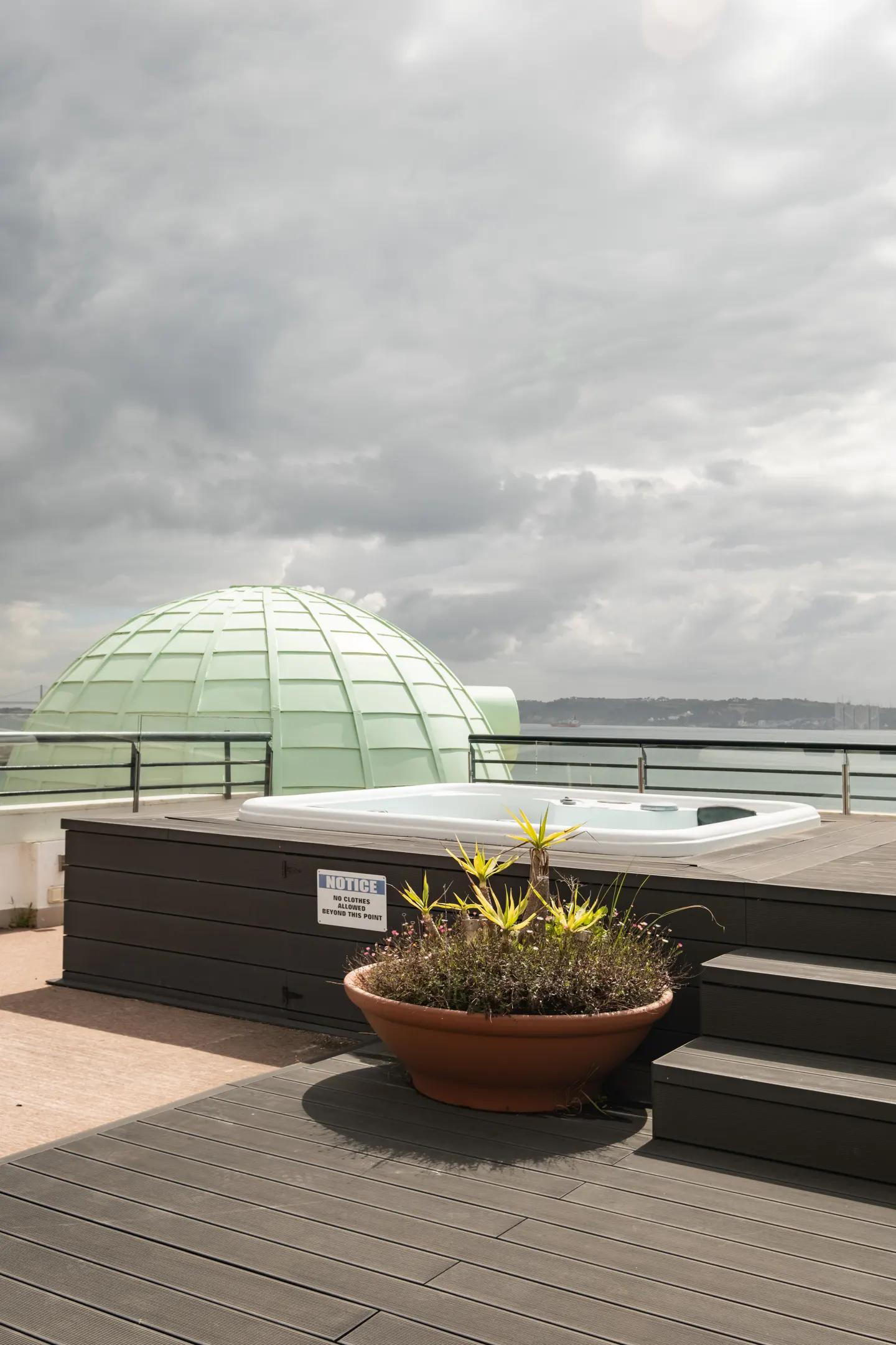 Rooftop deck with a hot tub, a green dome, and a terracotta pot with plants. The sky is cloudy.