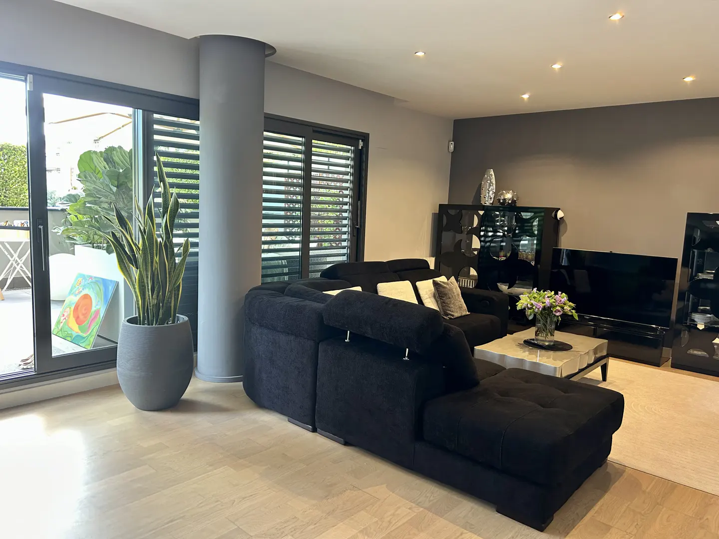 Living room with a black sectional sofa, marble coffee table, and a potted snake plant near sliding glass doors.