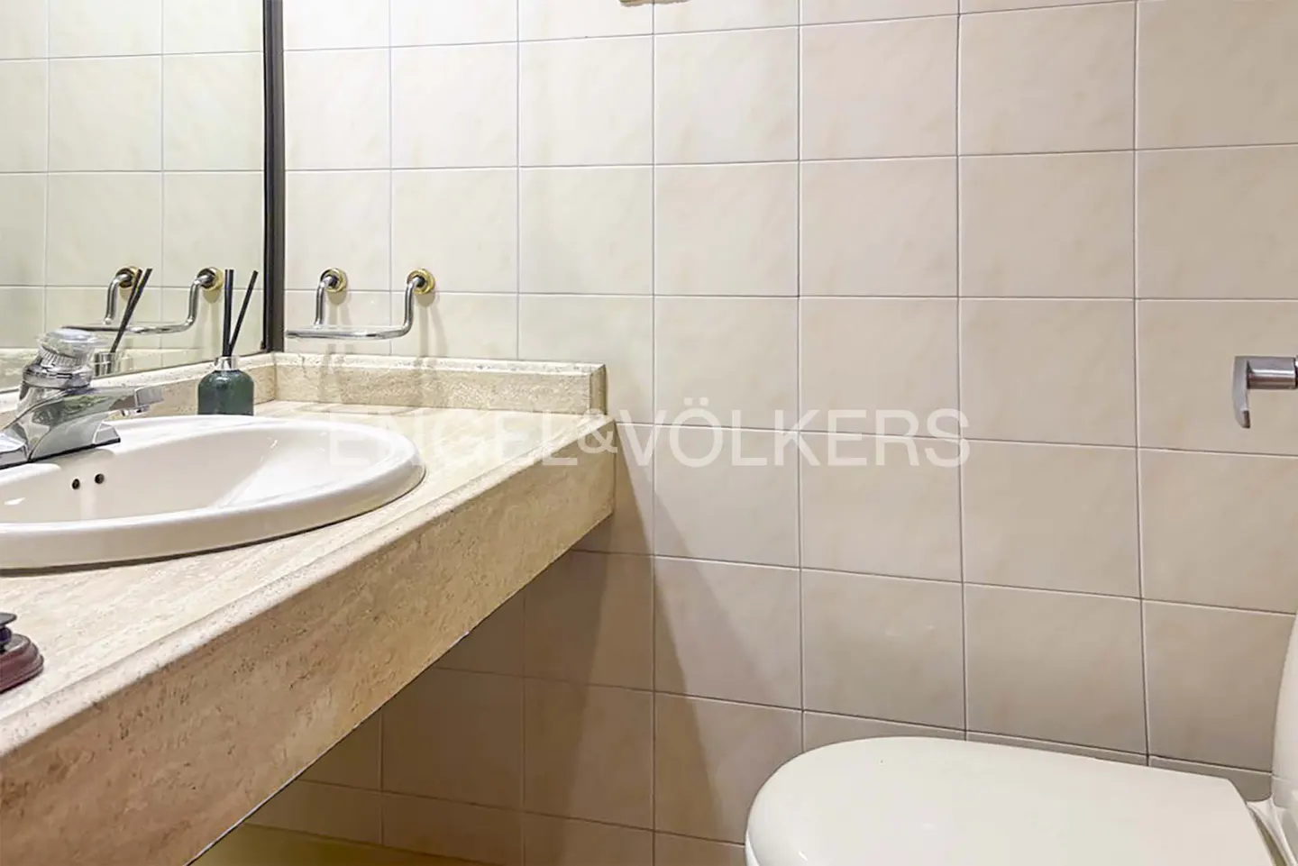Bathroom with a white sink, marble countertop, and a toilet. The walls are tiled in a light beige color.