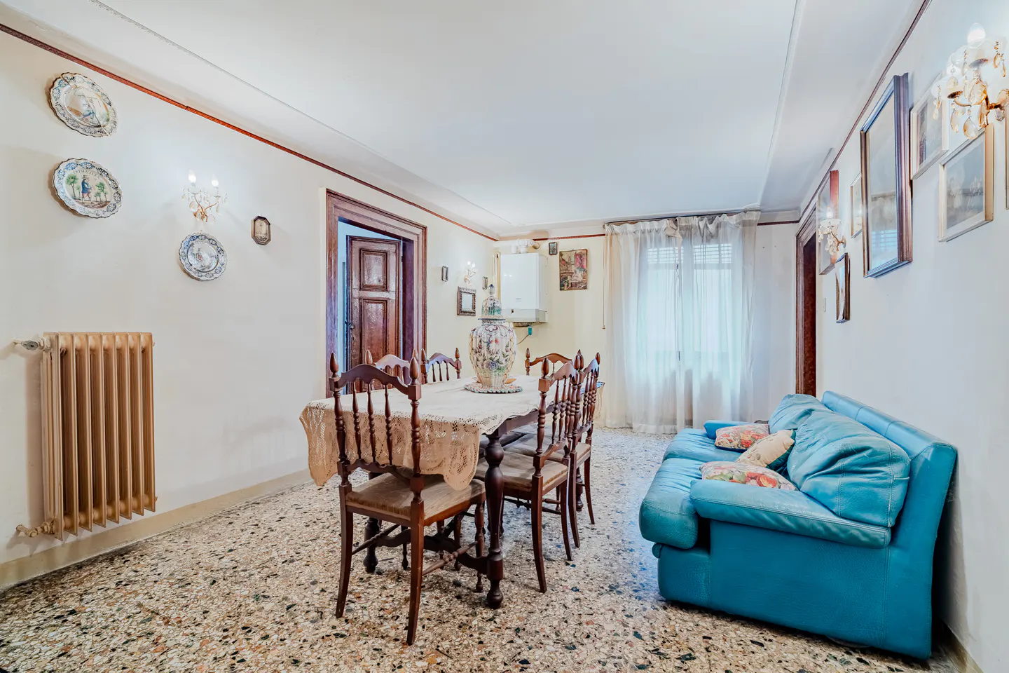 A dining room with a table, chairs, a blue sofa, and decorative plates on the wall.