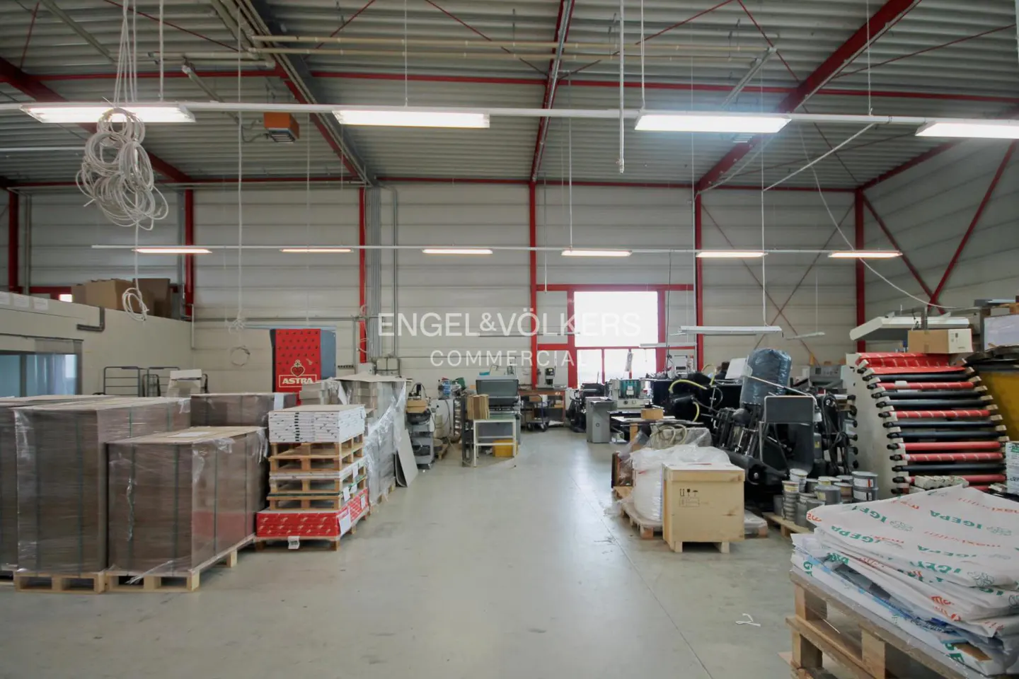 A wide shot of a large, empty warehouse with pallets of goods and machinery.