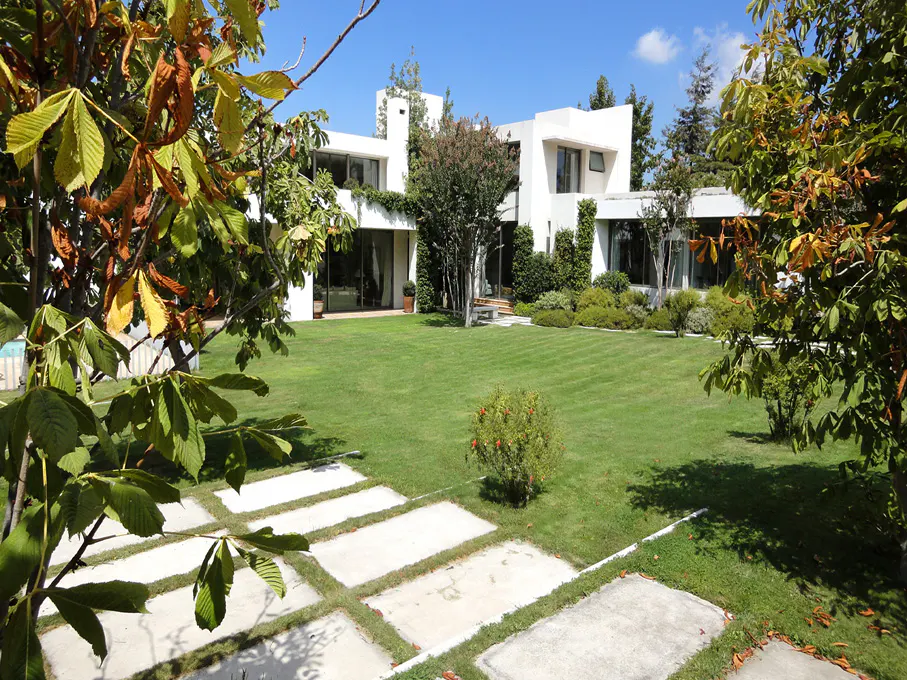 Modern white house with a green lawn and stone pathway on a sunny day. Trees frame the view.