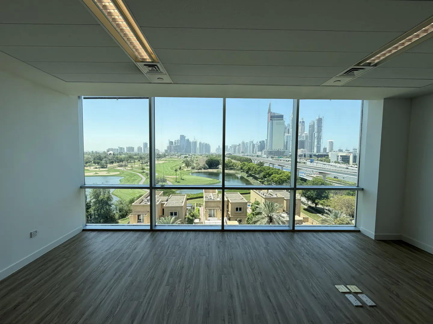 Empty office space with wood floors and a large window view of a golf course and city skyline.