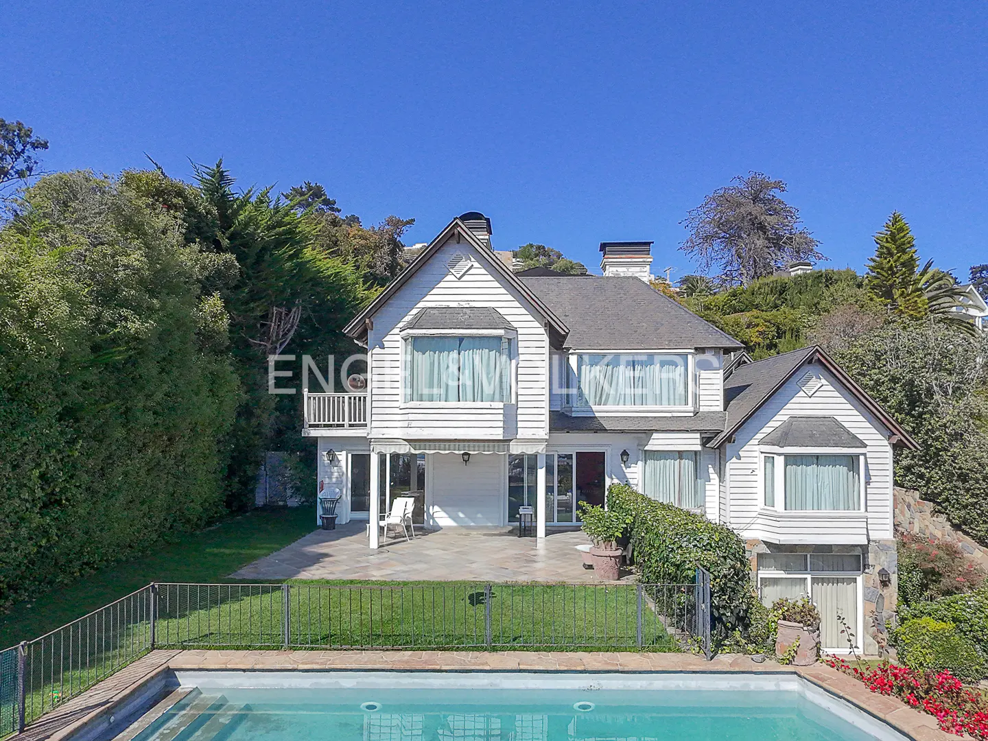Two-story white house with a pool, green lawn, and trees under a blue sky.