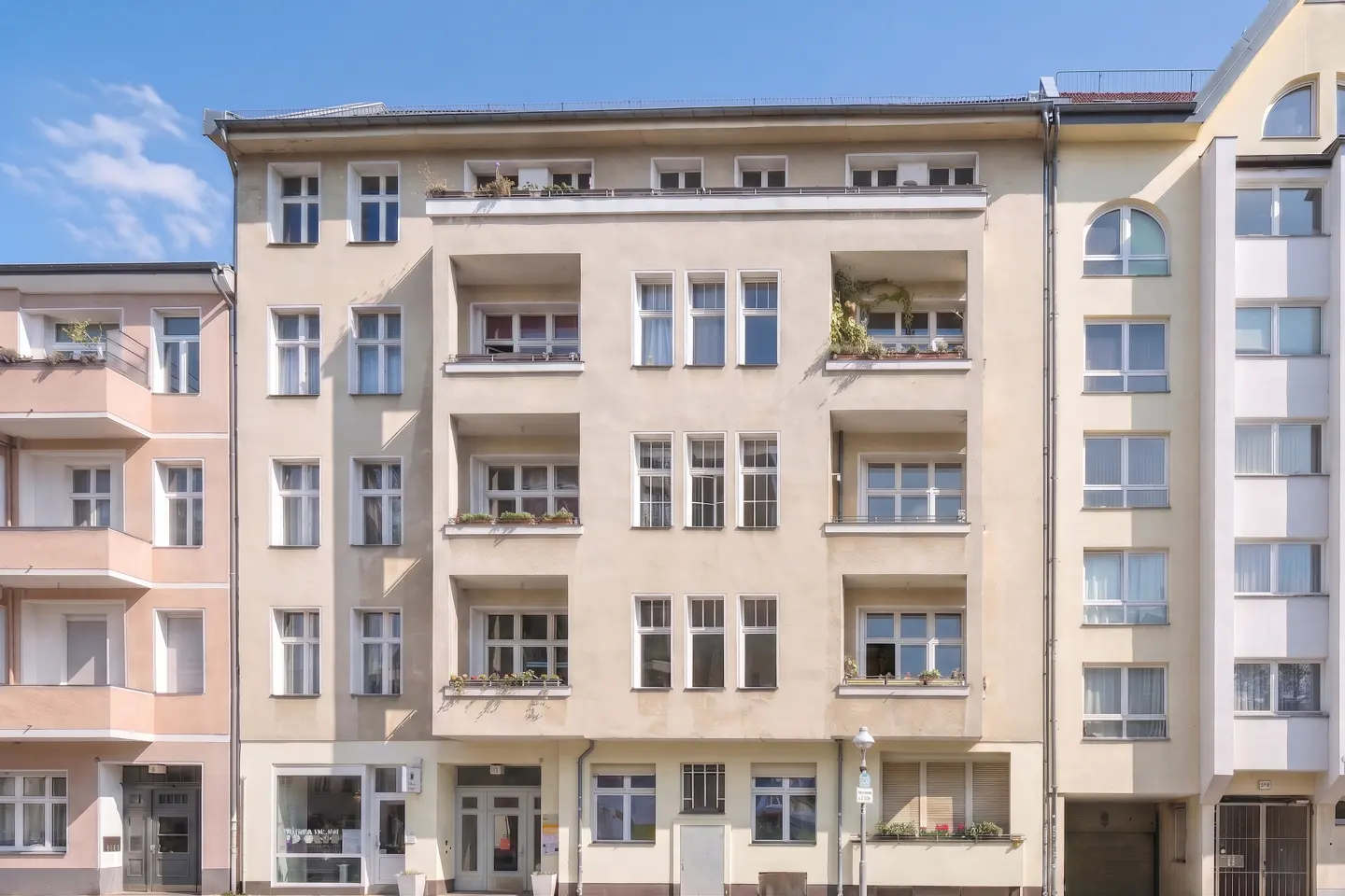A five-story apartment building with balconies and white-framed windows under a blue sky.